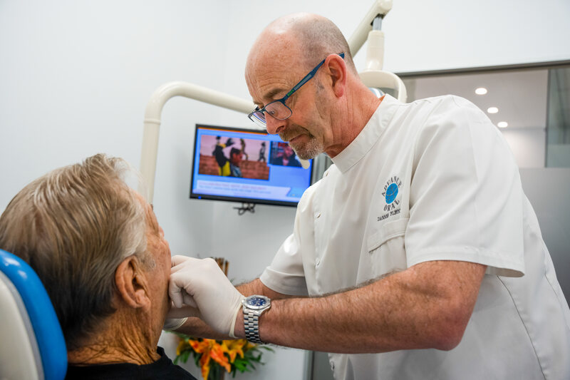 Specialist showing a mirror to a patient after inserting dental prosthetics, displaying a confident smile.